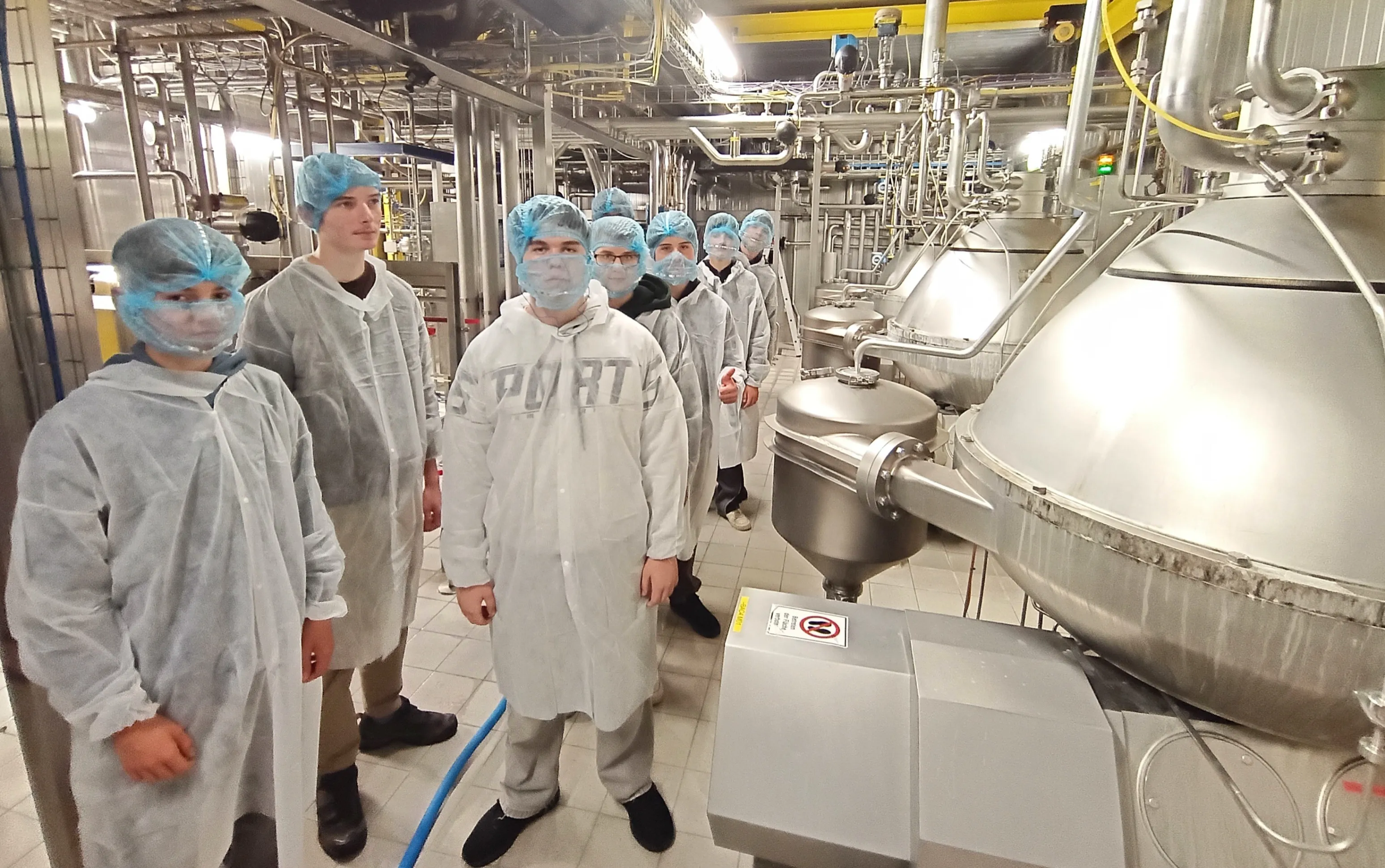Eine Gruppe von Menschen in Laborkittel und Masken steht in einer Fabrik.