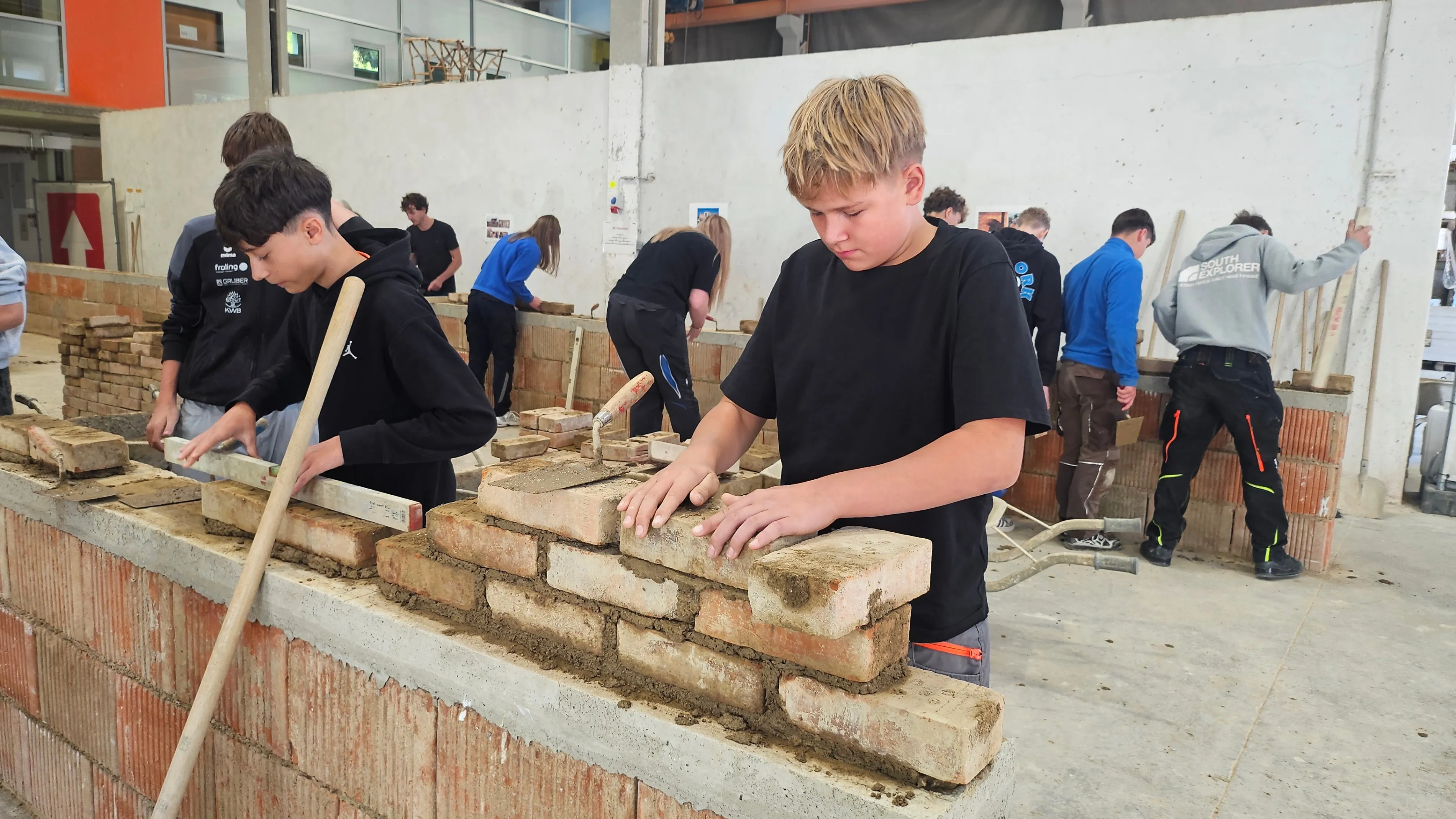 Eine Gruppe junger Menschen arbeitet gemeinsam daran, eine Ziegelmauer in einer Werkstatt zu bauen.