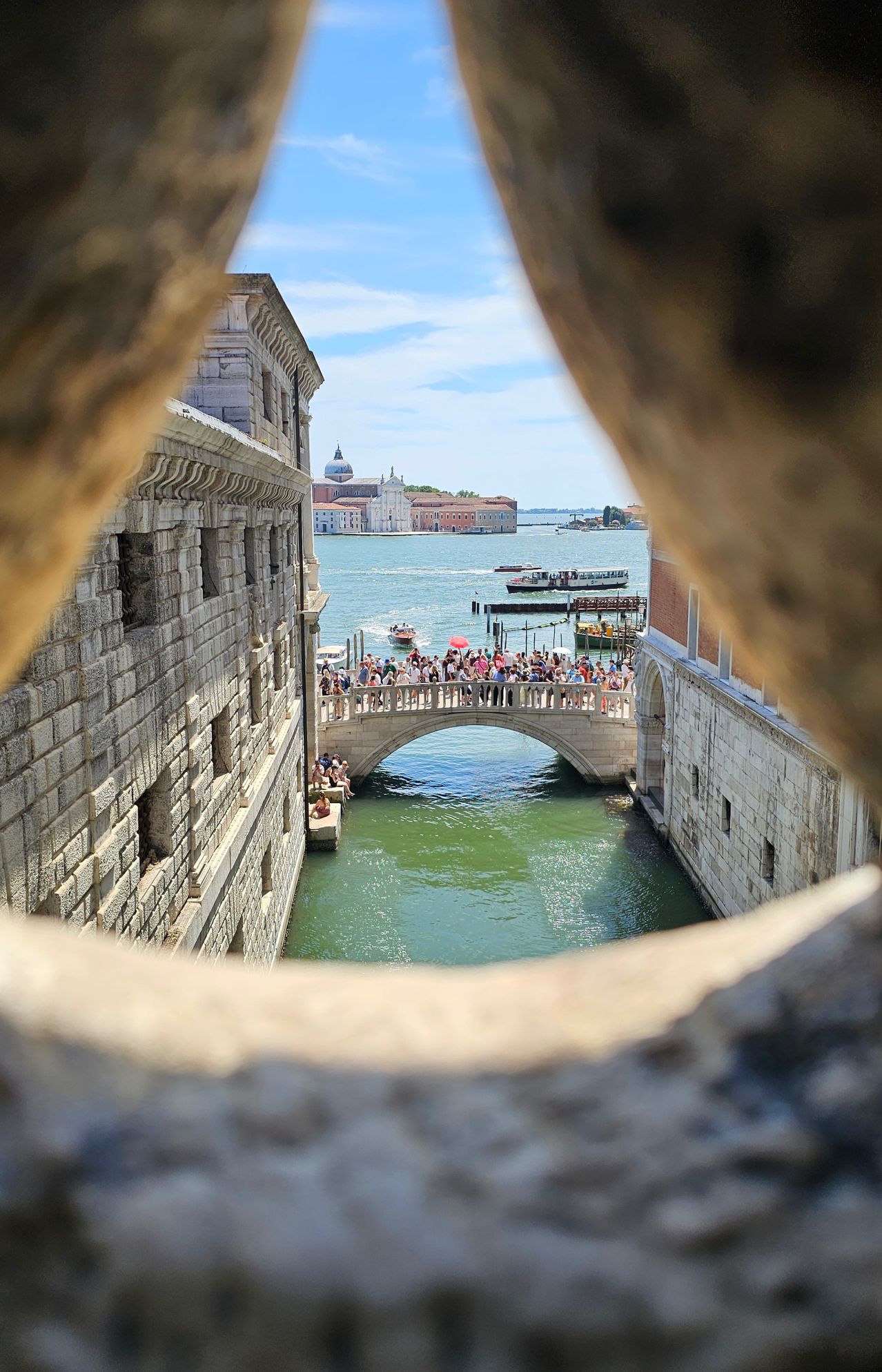 A view from a tower shows a bridge with many people and boats in the water. There are buildings on either side.