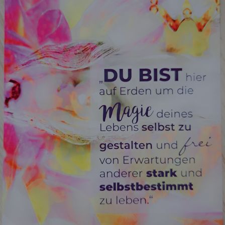 Ein motivierender Poster mit farbenfrohem Blumenhintergrund zeigt einen Spruch in fetter lila Schrift: 'DU BIST hier auf Erden um die Magie deines Lebens selbst zu gestalten und frei von Erwartungen anderer stark und selbstbestimmt zu leben.'