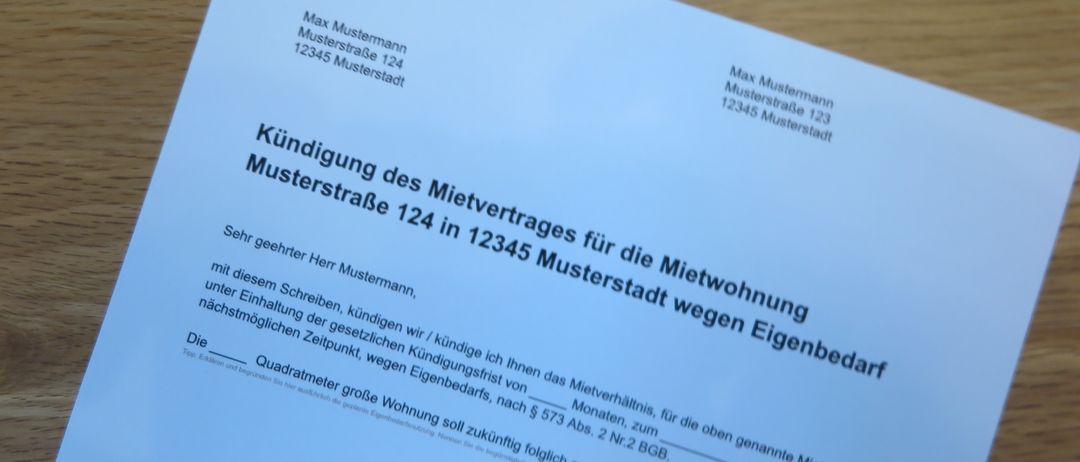 Ein weißes Dokument auf einer Holzoberfläche zeigt den Text 'Kündigung des Mietvertrages für die Mietwohnung Musterstraße 124 in 12345 Musterstadt'. Es enthält Adressen und einen Hinweis zur Kündigung eines Mietvertrags. Es ist an 'Max Mustermann' adressiert und erwähnt eine Kündigungsfrist und bestimmte Daten.