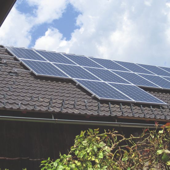 Ein Haus mit Solarpanelen auf dem Dach unter einem teilweise bewölkten Himmel.