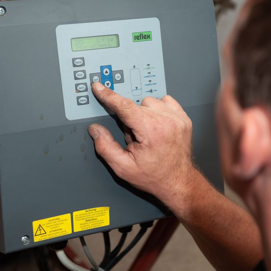Ein Mann drückt eine Taste an einer ReFlex-Maschine mit einem digitalen Display, das 2,8 bar und Intervalle anzeigt. Die Maschine hat gelbe Warnaufkleber.