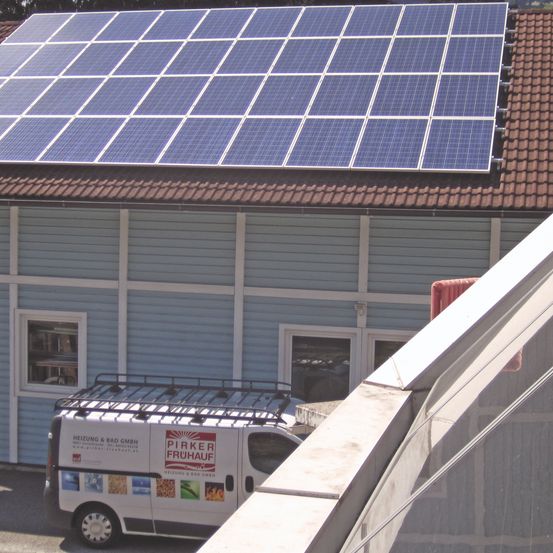Ein Gebäude mit einer Solarpanel-Anlage auf dem Dach. Ein weißer Van mit der Aufschrift 'Pirker Fruhauf' steht davor.