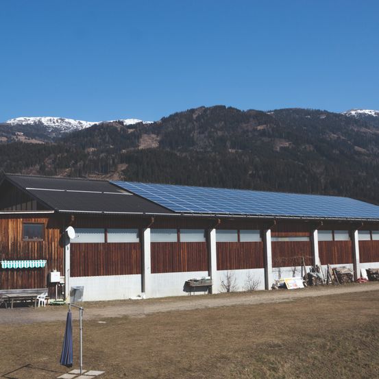 Ein Gebäude mit Solarmodulen auf dem Dach steht vor einer Bergkette unter einem klaren blauen Himmel.
