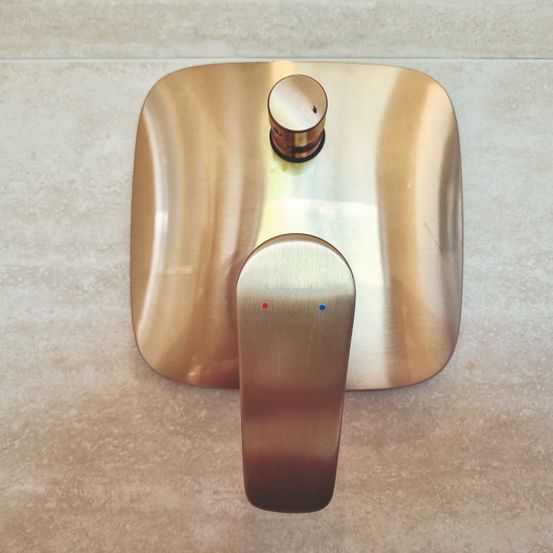 Ein Nahaufnahme eines modernen Messinghahns, montiert an einer gefliesten Wand, mit einem eleganten Griff und einem dekorativen Knopf.