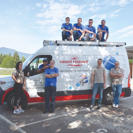 Eine Gruppe von Fachleuten posiert vor einem weißen Van mit Solarmodulen auf dem Dach, sie tragen blaue Hemden und Hosen.