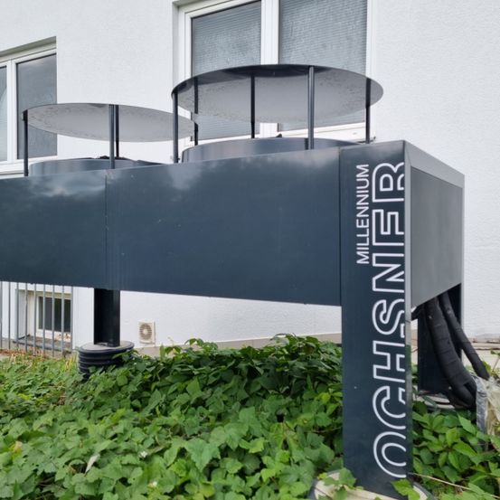 Eine graue Außenstruktur mit den Worten Millennium und Ochsner davor steht vor einem weißen Gebäude mit Glasfenstern.