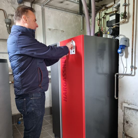 Ein Mann in einer blauen Jacke und Jeans inspiziert ein rot-schwarzes Gerät in einem Hauswirtschaftsraum.