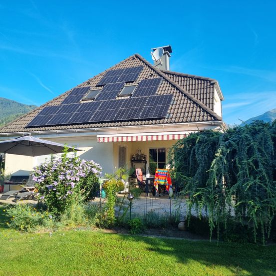 Ein sonniger Tag mit Solarmodulen auf dem Dach eines Hauses mit Garten und Terrasse.