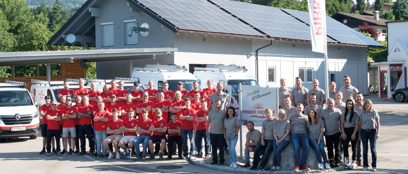 Eine Gruppe von Menschen in identischen Hemden posiert vor einem Gebäude mit Solarpanelen. Das Schild heißt 'Pirker Fruit'.
