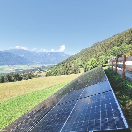 Solarpanele sind auf einem Hang mit Blick auf Berge und ein Dorf installiert.