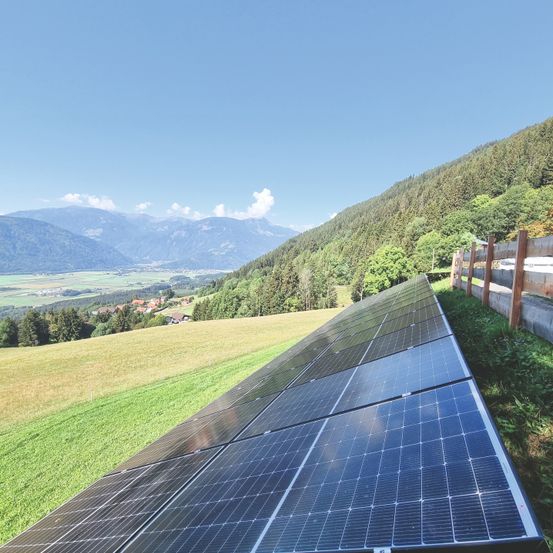 Solarpanele sind auf einem Hang mit Blick auf Berge und ein Dorf installiert.