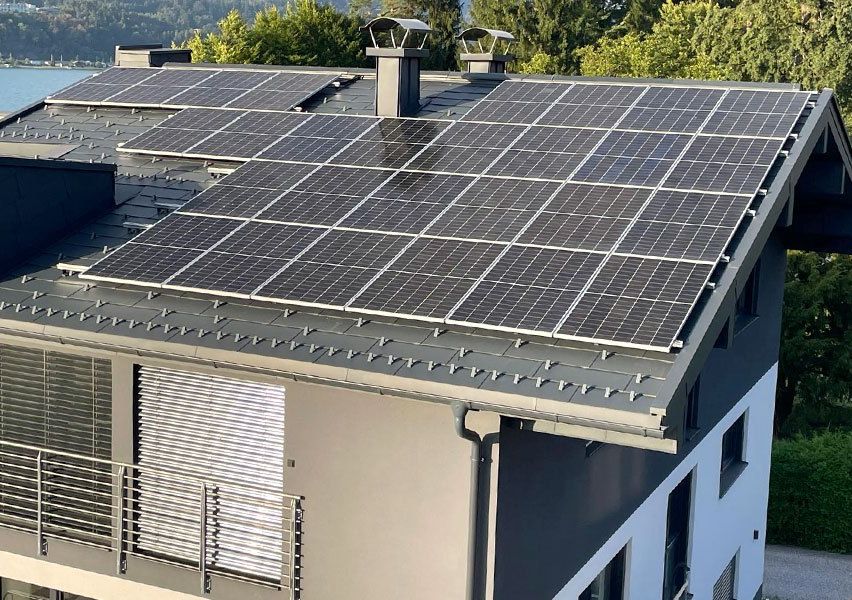 Ein Haus mit einer großen Solarpanel-Installation auf dem Dach, mit Blick auf einen See und umgeben von Bäumen.