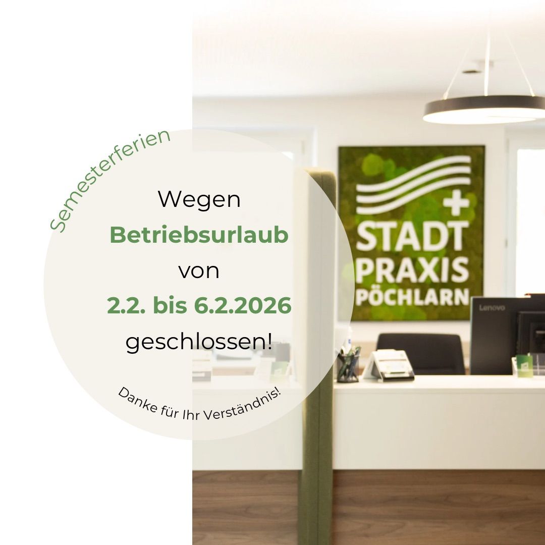 Ein weißer Raum mit einem grünen Banner, das 'Semesterferien' und 'Wegen Betriebsurlaub von 2.2. bis 6.2.2026 geschlossen!' besagt. Ein weißer Schreibtisch mit Computer und Monitor ist sichtbar. Der Raum hat eine weiße Decke und Wände.