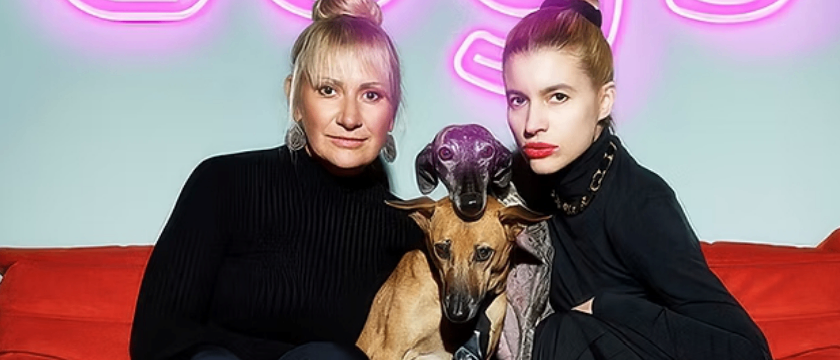 Zwei Frauen und ein Hund sitzen auf einem Sofa. Das Schild über ihnen sagt 'dogs'. Darunter stehen die Namen Angelika Niedezky und Lisa-Lena Tritscher.