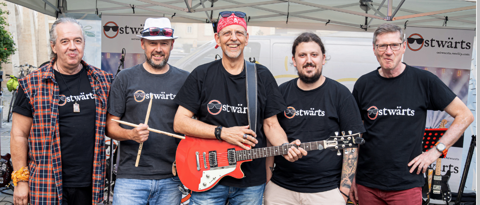 Fünf Männer posieren vor einem Zelt für ein Open-Air-Konzert mit der Band Ostwärts, einer Kurt Ostbahn Tribute Band.