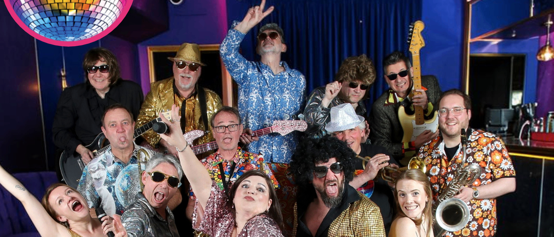Disco Review Band, gekleidet in Disco-Kleidung, posiert für ein Foto in einer Disco-Umgebung, mit Musikinstrumenten und einer Discokugel im Hintergrund.