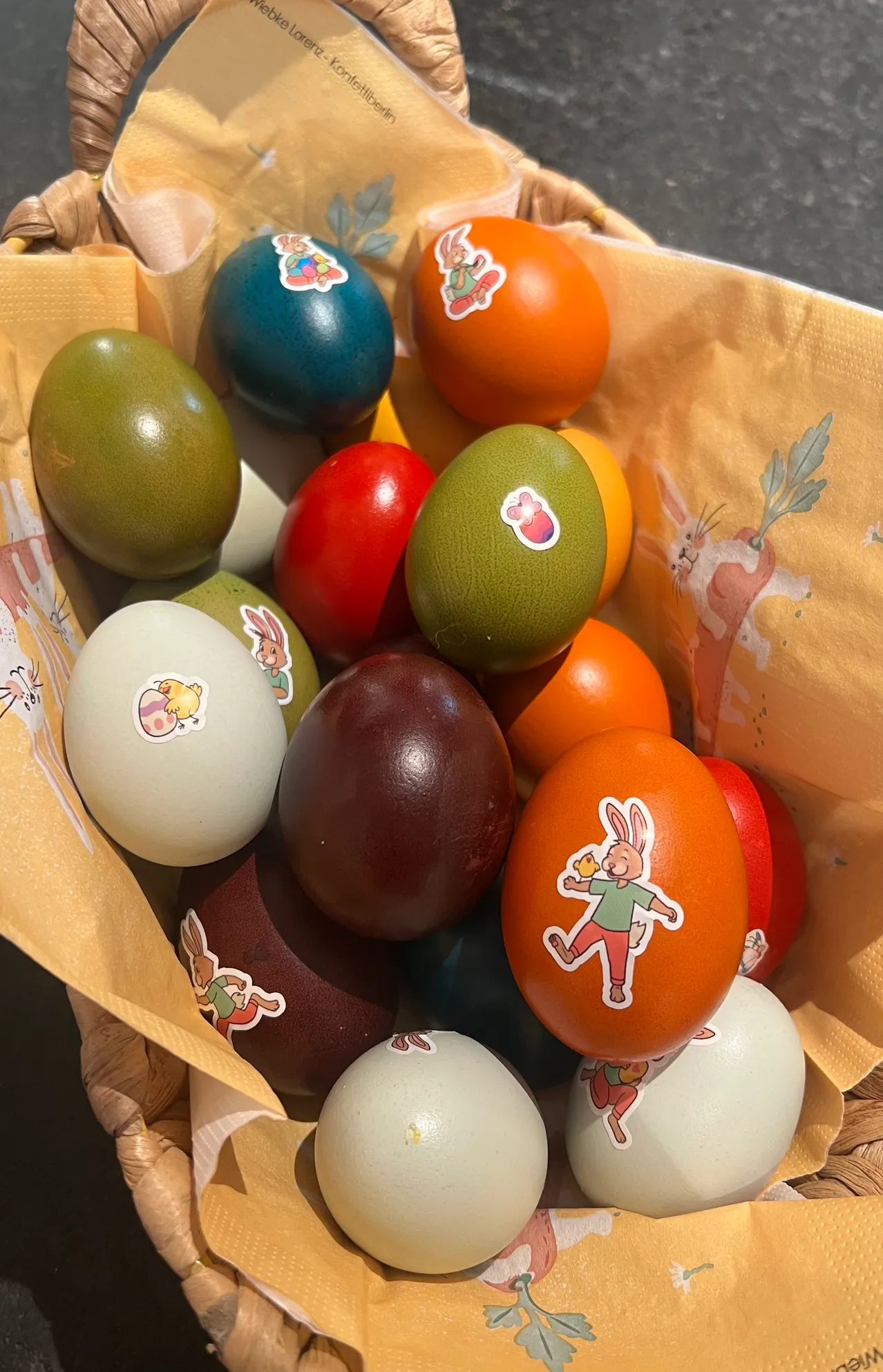 Ein Korb voller bunter Ostereier mit Hasenaufklebern. Die Eier sind in verschiedenen Farben und Größen.
