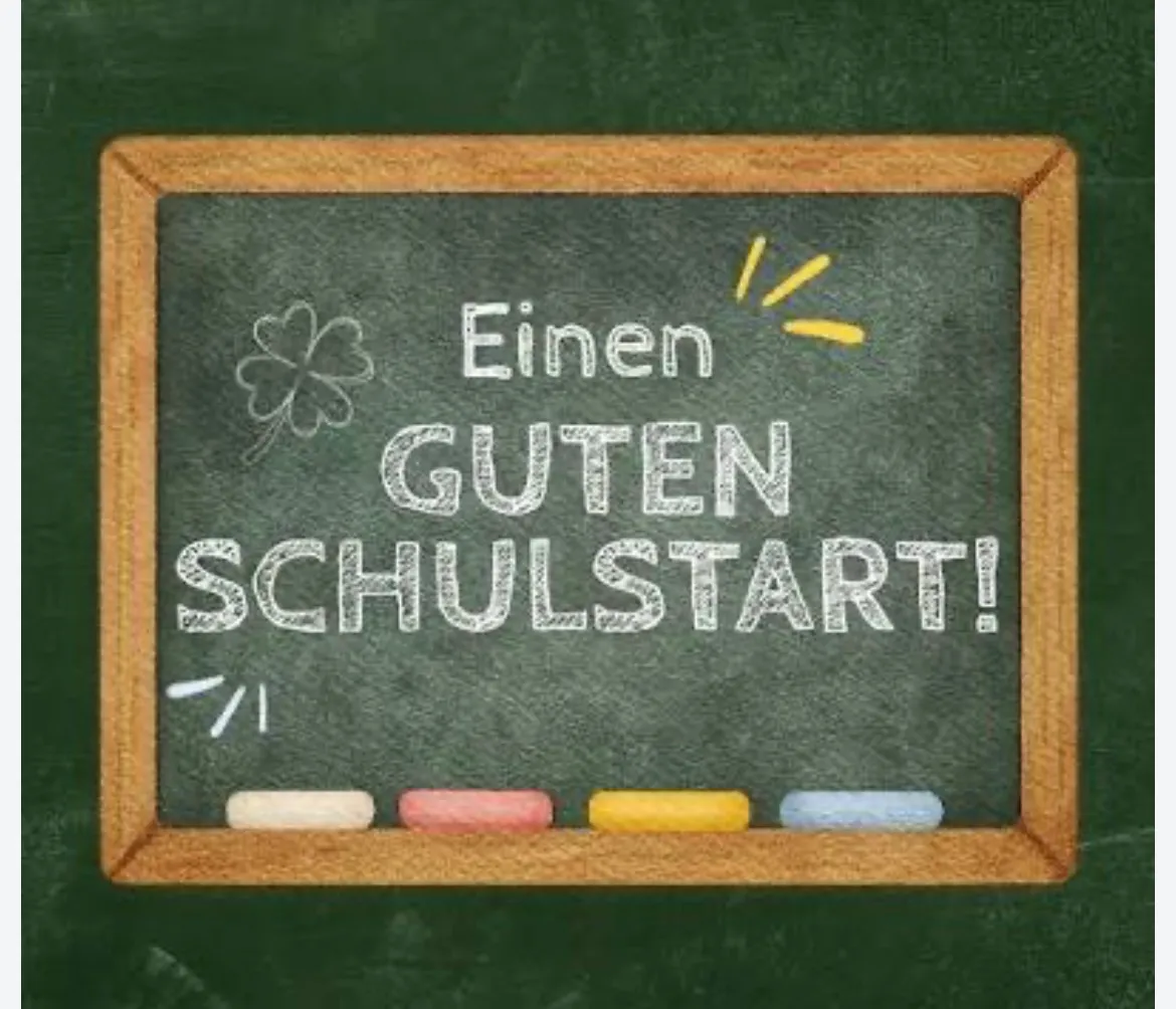Ein Schultafel mit der Aufschrift 'Einen Guten Schulstart!' in weißer Kreide geschrieben. Ein gelber Sonnenstrahl und ein grünes Kleeblatt sind ebenfalls gezeichnet. Unten befinden sich vier farbige Kreiden.