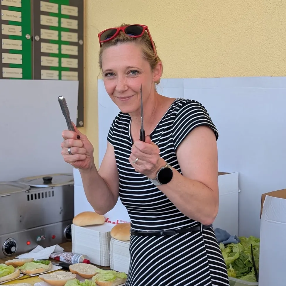 Eine Frau in einem schwarz-weißen Kleid hält eine Zange und ein Messer vor einem Tisch mit Sandwiches.