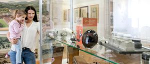 Eine Frau und ein Kind stehen vor einer Vitrine mit alten elektrischen Geräten in einem Museumsraum.