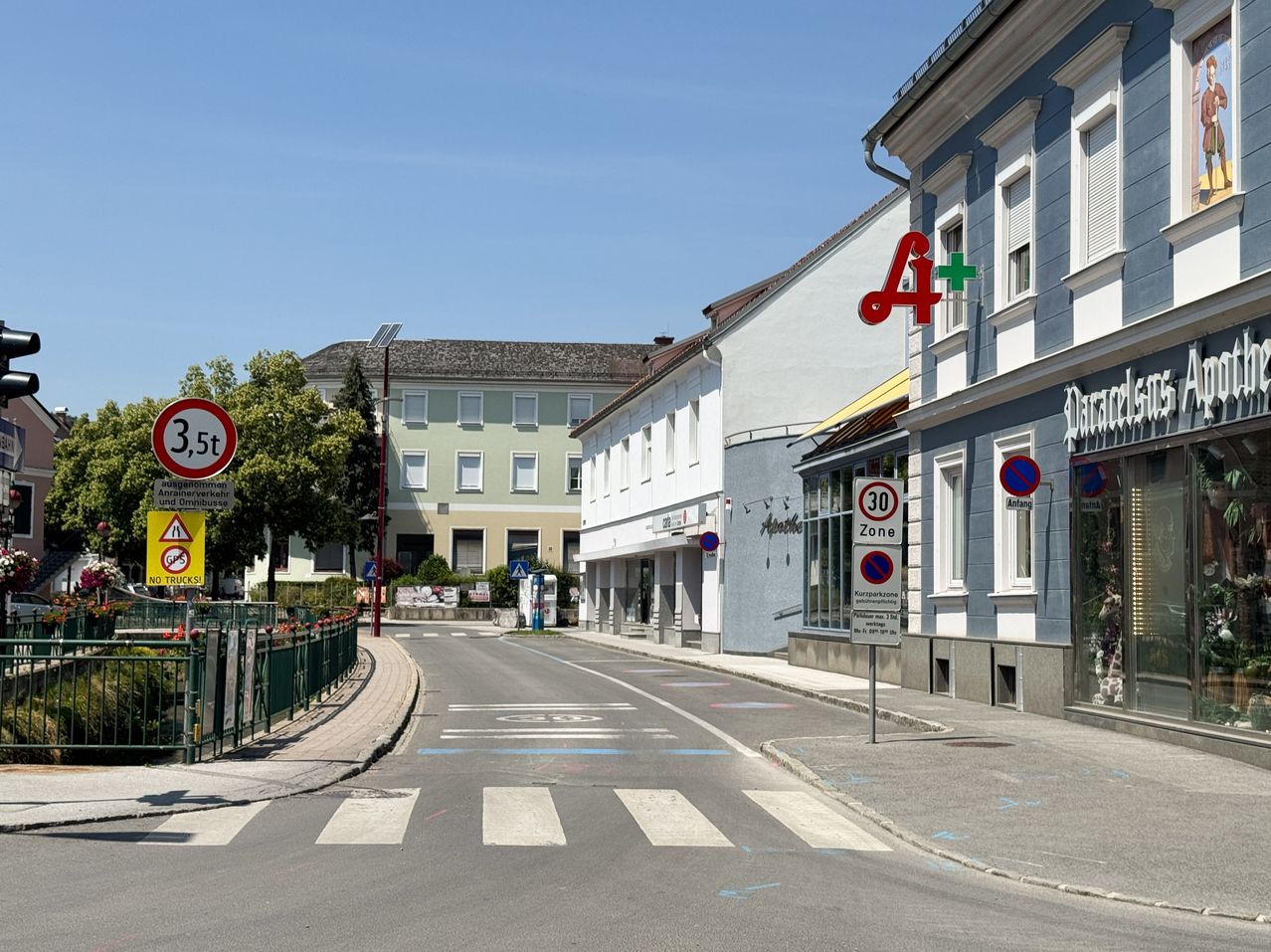 Eine leere Straße mit Gebäuden auf beiden Seiten, eines hat ein Schild mit einem roten Buchstaben A und einem Pluszeichen. Ein Verkehrsschild auf der linken Seite sagt 3,5. Auf der rechten Seite befindet sich ein Gebäude mit einem Schild, das 30 Zone anzeigt.
