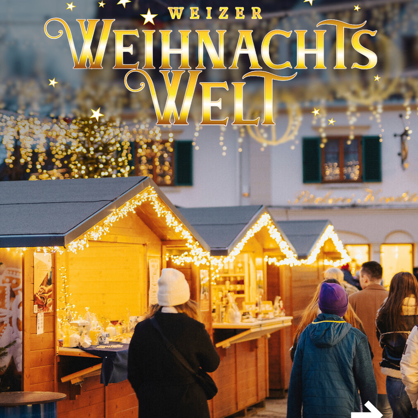 Ein Weihnachtsmarkt im Freien mit Holzhütten, Lichterketten und Leuten beim Erkunden. Im Hintergrund steht ein Gebäude mit Lichtern und Dekorationen.