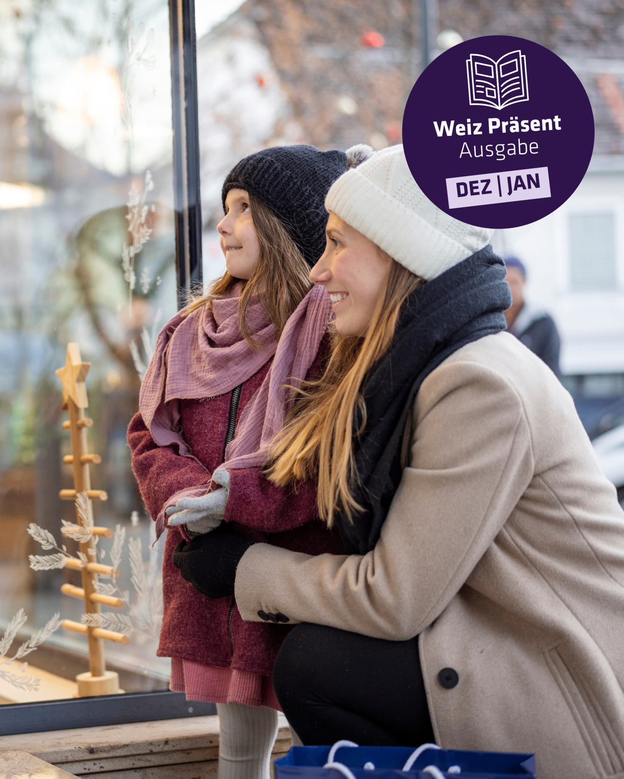 Zwei Frauen und ein junges Mädchen stehen lächelnd vor einem Fenster. Das Mädchen trägt einen lila Schal und eine schwarze Mütze. Sie tragen Winterkleidung. Dahinter ist ein unscharfer Hintergrund einer Straße und eines Autos.