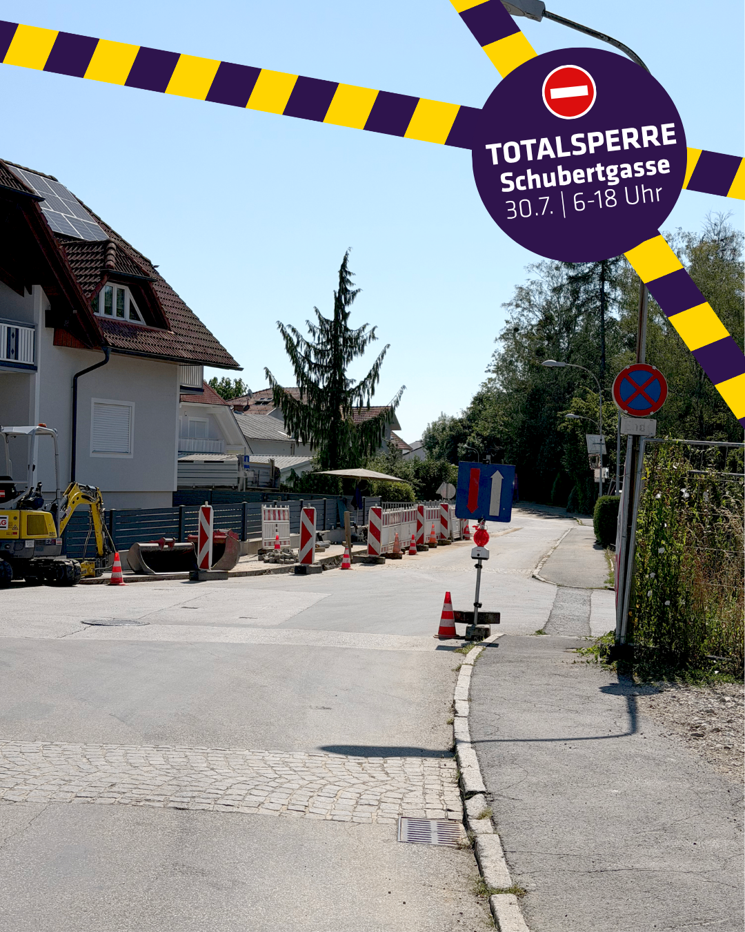 Eine Straße im Bau mit einem Totalsperrschild, einem gelben Bagger und Verkehrskegeln an der Seite. Solarmodule sind auf dem Dach eines Hauses.