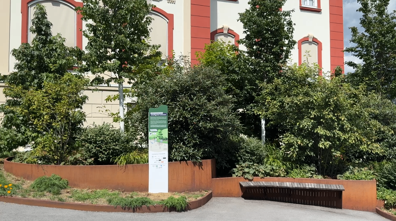 Ein Garten mit einem Schild in der Mitte, umgeben von Bäumen und einem Gebäude mit rotem Rand.