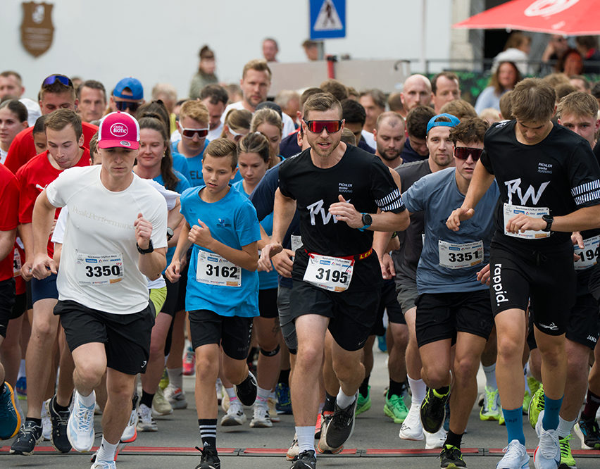 Läufer bei einem Marathon stellen sich zum Start auf. Einige tragen Sonnenbrillen und Nummern. Der Mann vorne trägt eine rosa Mütze.