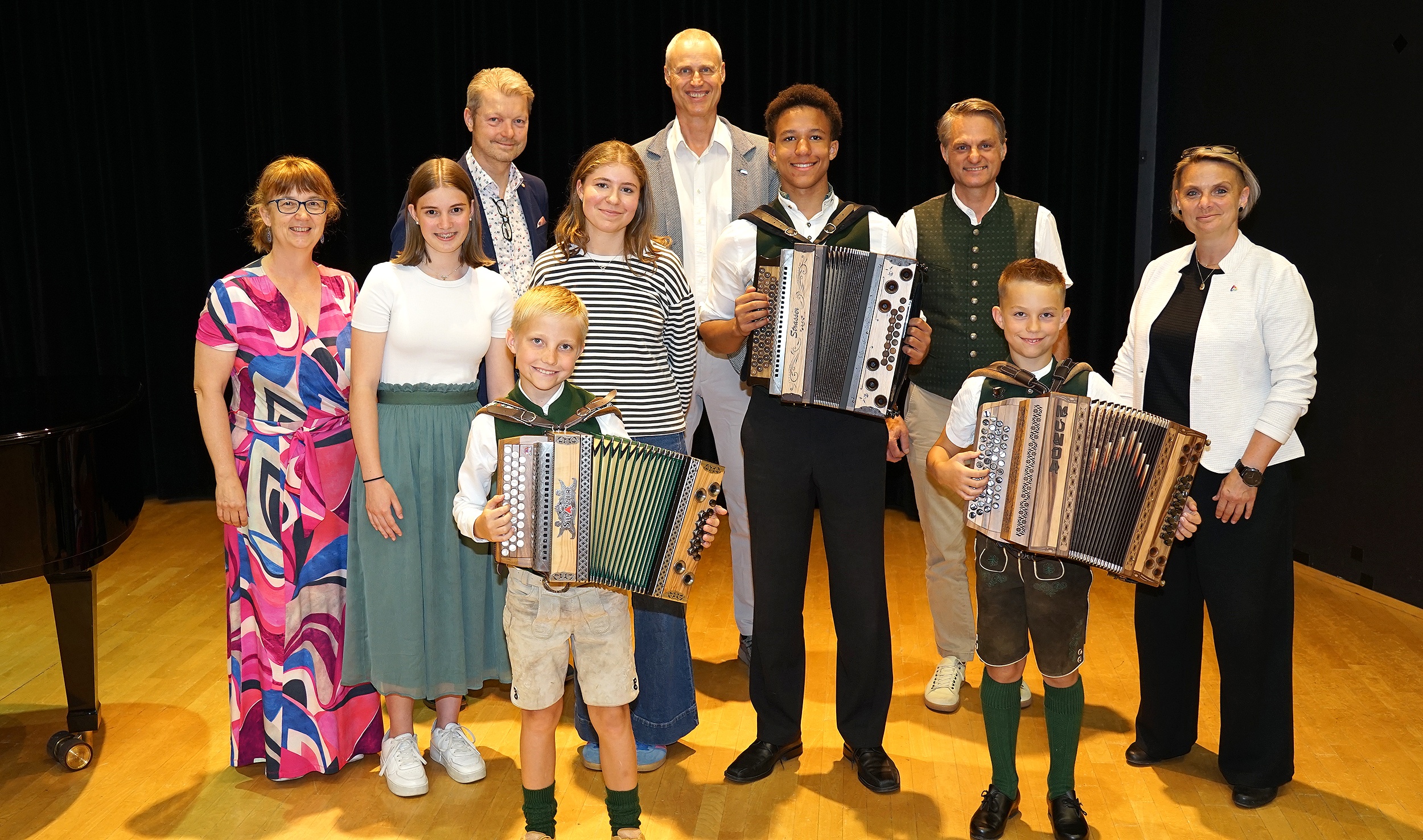 Kinder mit Harmonikas und Erwachsene stehen auf einer Bühne in Österreich.