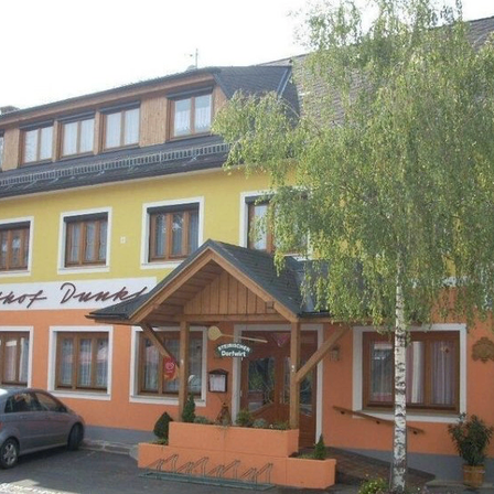 Ein gelbes und oranges Gebäude mit mehreren Fenstern, einem geparkten Auto davor und einem Baum vor dem Eingang.