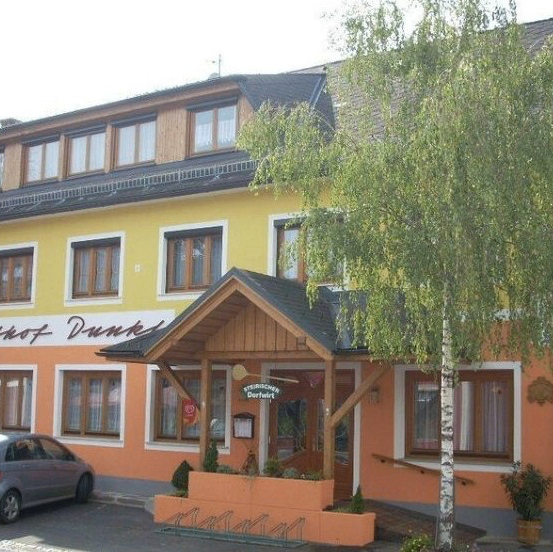 Ein gelbes und oranges Gebäude mit mehreren Fenstern, einem geparkten Auto davor und einem Baum vor dem Eingang.