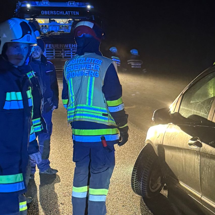 Einsatzkräfte in Reflektorwesten stehen bei Nacht neben einem Fahrzeug. Die Szene wird von blinkenden Lichtern beleuchtet.