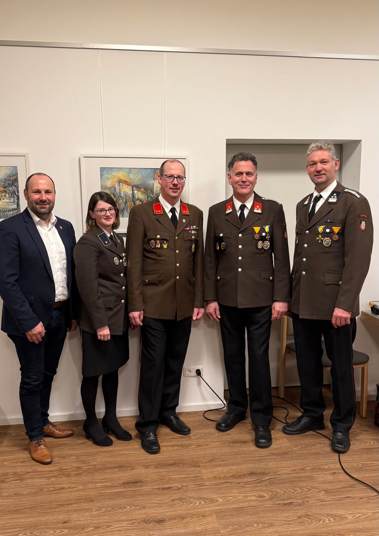 Fünf Personen, darunter vier in Militäruniformen und eine in einem Anzug, stehen gemeinsam in einem Raum. Sie scheinen für ein Foto zu posieren.