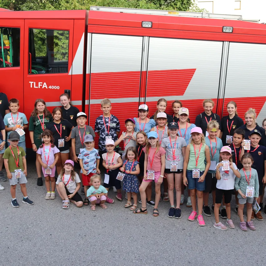 Eine Gruppe von Kindern und Erwachsenen posiert für ein Foto vor einem roten Feuerwehrauto mit der Nummer 4000. Sie tragen Namensschilder und einige tragen Hüte.
