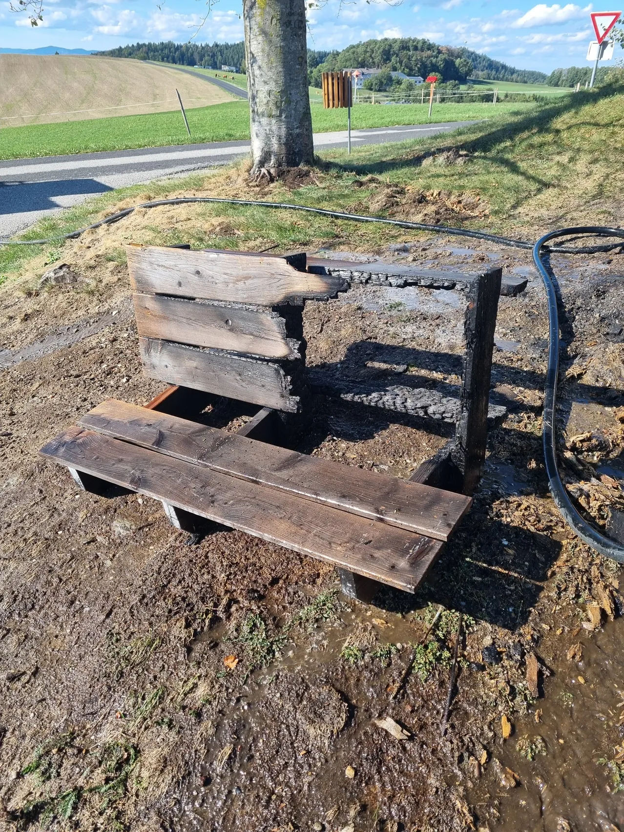 Eine hölzerne Bank in einem Park wurde durch Feuer beschädigt, mit verkohltem Holz und Brandflecken.