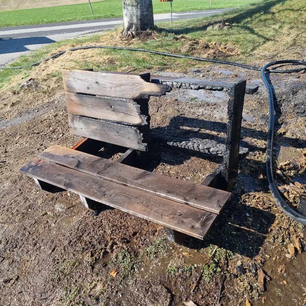 Eine hölzerne Bank in einem Park wurde durch Feuer beschädigt, mit verkohltem Holz und Brandflecken.