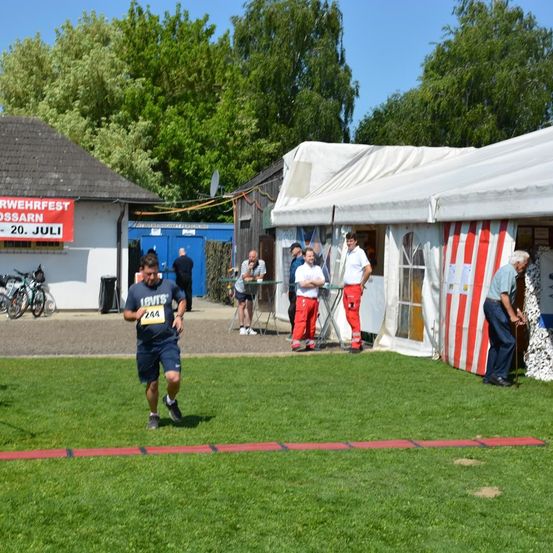Ein Marathonläufer mit der Nummer 244 läuft auf einem Rasenfeld. Hinter einem weißen Zelt stehen mehrere Personen.