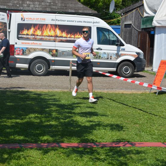 Ein Läufer mit der Nummer 29 joggt vor einem Feuerwehr-Van. Eine Person geht hinter dem Van.