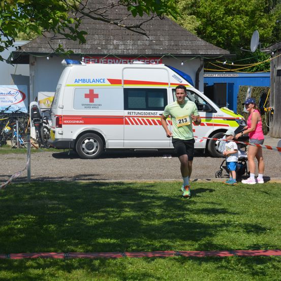 Ein Mann mit der Nummer 213 läuft vor einem Krankenwagen bei einem Rennen, in der Nähe einer Familie.