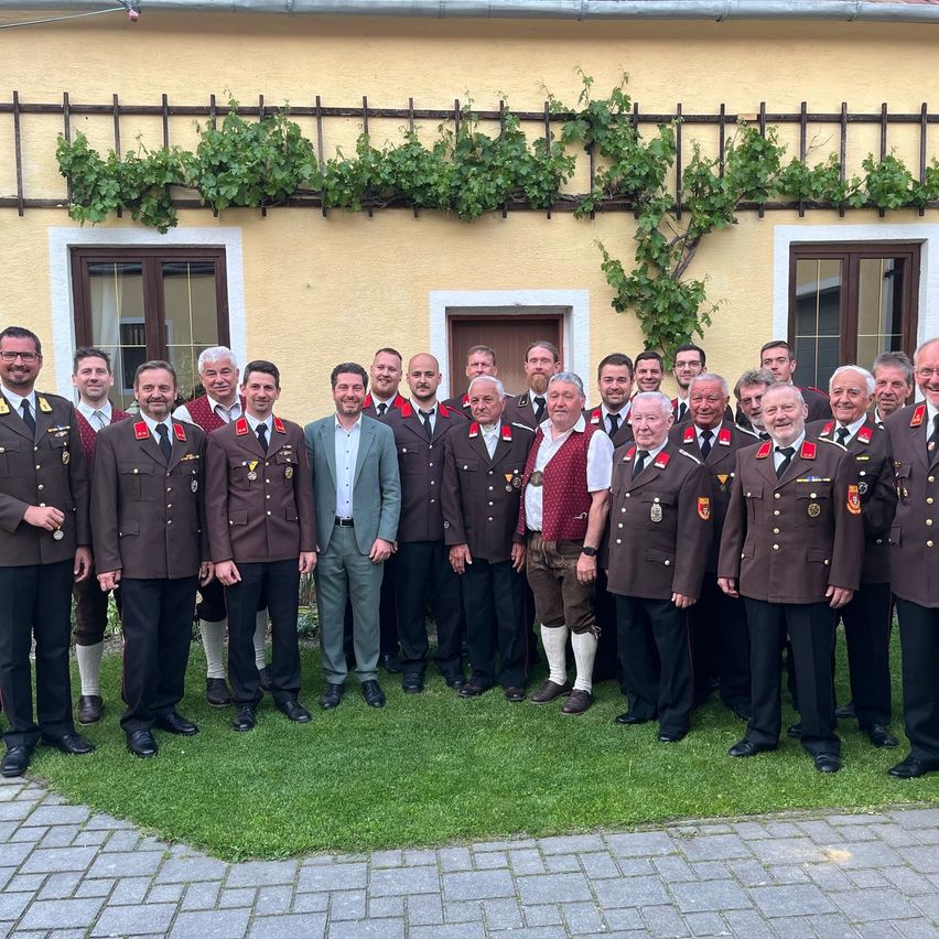 Eine Gruppe von Männern in Uniformen, einige in traditioneller Kleidung, posiert für ein Foto vor einem gelben Gebäude mit Weinreben.