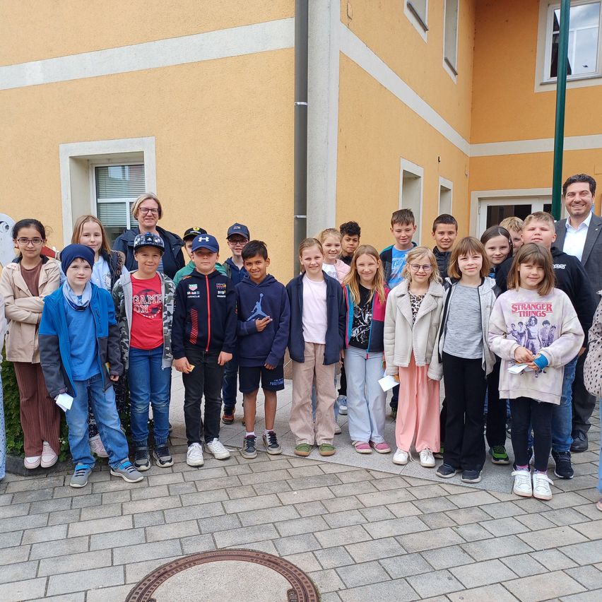 Eine Gruppe von Kindern und Erwachsenen steht vor einem gelben Gebäude mit weißen Akzenten. Sie alle lächeln und scheinen für ein Foto zu posieren.