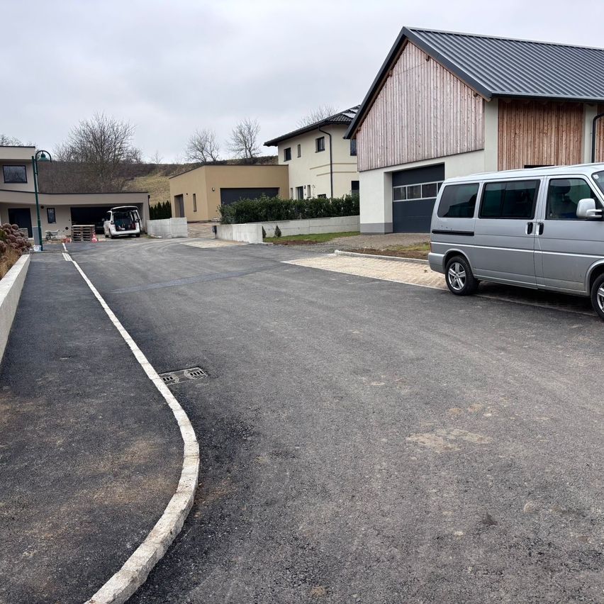 Ein neuer Einfahrtsweg vor zwei Häusern, eines mit einem Metalldach, und ein silberner Van auf der Seite geparkt.