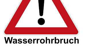 Ein rotes und weißes Warnschild mit schwarzem Ausrufezeichen und dem Text 'Wasserrohrbruch' darunter.