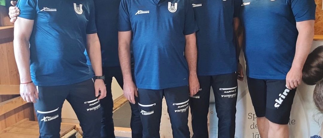 Fünf Männer in blauen Hemden und schwarzen Shorts posieren für ein Foto vor einer Wand mit dem Schild ESV Gossnitz. Sie tragen alle Turnschuhe.