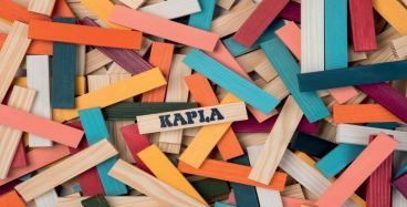 Eine farbenfrohe Ansammlung von Holzstäbchen in verschiedenen Farben, wobei einer das Wort 'KAPLA' in fetten, schwarzen Buchstaben hervorsticht.