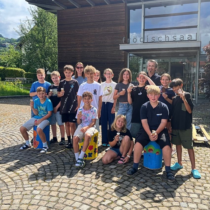 Eine Gruppe von Kindern und zwei Erwachsenen lächelt und posiert für ein Foto vor einem Gebäude. Sie alle haben Eis in den Händen.